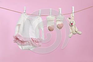 Baby clothes and handmade toy drying on washing line against pink background