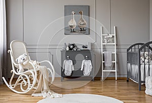 Baby clothes hanging on knobs on grey wooden commode in lovely nursery, copy space and poster on empty wall photo