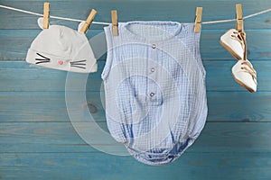 Baby clothes hanging on washing line near light blue wooden wall