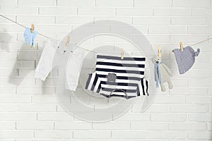 Baby clothes hanging on washing line near white brick wall