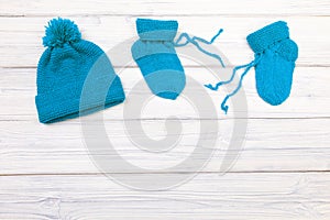 Baby clothes knitted booties and hat on a white wooden background. View from above - Image