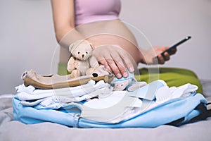 Baby clothes, necessities for mother and newborn in maternity bag. Pregnant woman getting ready for labor packing stuff for