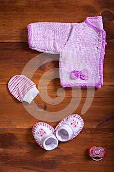 Baby clothes pink knitted sweater cotton mittens socks and dummy on wooden background, infant cloth set on table, child newborn