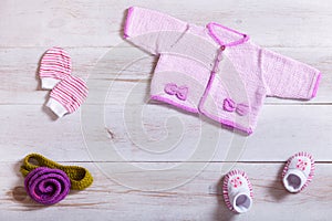 Baby clothes pink knitted tiny sweater cotton little mittens socks on white wooden background, infant cloth set on table, child