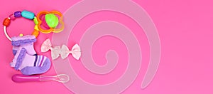 Baby clothes, rattles, feeding spoon on pink background. Horizontal banner. Copy space for text