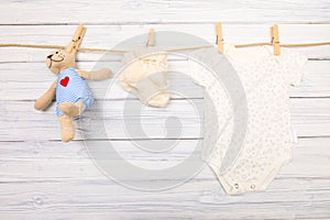 Baby clothes and  toy bear on a clothesline on wooden background  - Image