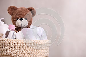 Baby cosmetic products, bath accessories and toy bear in knitted basket on beige background, closeup. Space for text