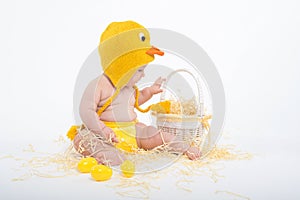 Baby in a costume of chicken looking intently in white wicker basket with hay