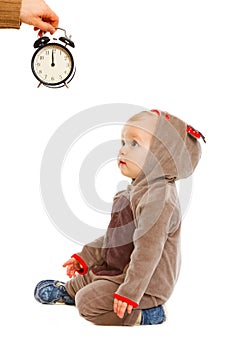 Baby in costume looking on alarm clock