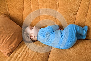 Baby on the couch. Happy baby lay idle. Portrait of a lovely laughing and blue shirt lying on a couch and looking up