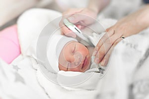 Baby in the crib measures body temperature. Mom measures the baby`s body temperature with a thermometer.