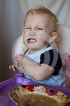 Baby cries and refuses to eat soup. The little white boy waves his hand away from the food