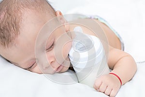 Baby curled up sleeping on a blanket with feeding bottle