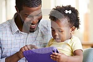 Baby Daughter And Father Playing With Toy On Sofa In Lounge At Home