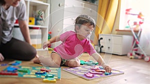 Baby daughter plays with toys on the floor develops fine motor skills. Mom plays with her baby daughter, teaches her to