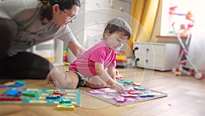 Baby daughter plays with toys on the floor develops fine motor skills. Mom plays with her baby daughter, teaches her to