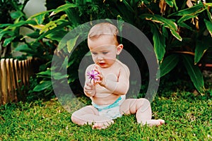 Baby in diaper without clothes sitting on the grass nibbling a flower