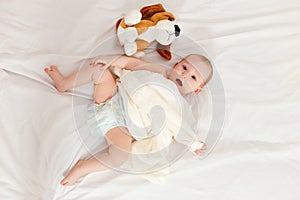 Baby in diaper lies on her back on the bed