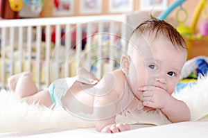 Baby in diaper lying against white bed