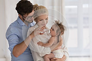 Baby in diaper on parents arms drinks water from bottle