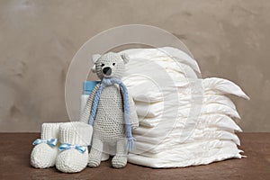 Baby diapers, toy bear and child`s booties on table