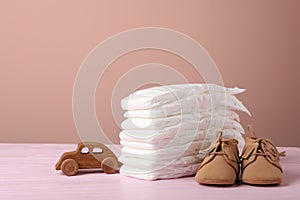 Baby diapers, toy car and child`s shoes on wooden table against pink background