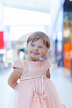 Baby in a dress smiles, on the background of a shopping center