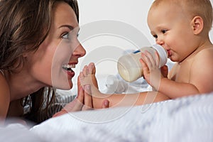 Baby drinking from bottle with mother smiling