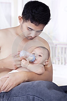Baby drinking milk with dad in bedroom