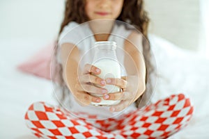 The baby is drinking milk. A little girl at home on the bed drinks yogurt.