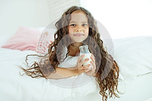 The baby is drinking milk. A little girl at home on the bed drinks yogurt.
