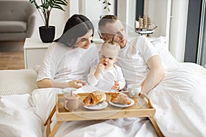 Baby drinking from sippy cup while parents snuggling at home