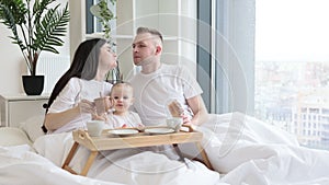 Baby drinking from sippy cup while parents snuggling at home