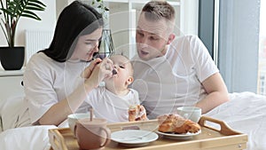 Baby drinking from sippy cup while parents snuggling at home