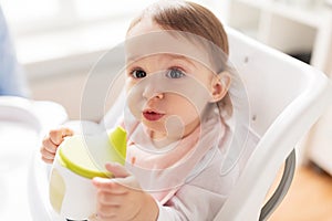 Baby drinking from spout cup in highchair at home