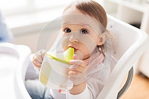 Baby drinking from spout cup in highchair at home