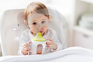 Baby drinking from spout cup in highchair at home