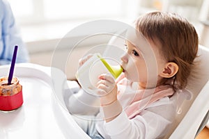 Baby drinking from spout cup in highchair at home
