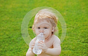 Baby drinking water. Close-up of child baby drinking fresh and pure water from bottle with a blurred green grass