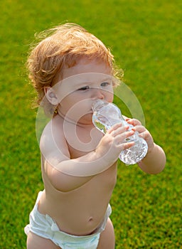 Baby drinking water. Close-up of little blonde child drinking fresh and pure water from bottle with a blurred green