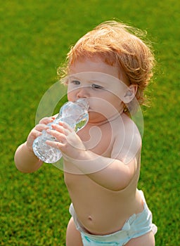 Baby drinking water. Close-up of little blonde child drinking fresh and pure water from bottle with a blurred green