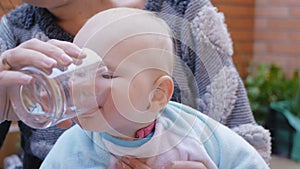 Baby drinking water from glass from hands of mother