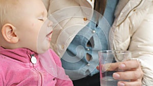 Baby drinking water from glass from mother`s hand