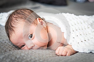 Baby with earring looking at camera reclining with a blanket on the bed