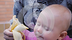 Baby eating banana from hands of mother