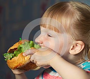 Baby eating a big fast food hamburger with a lot of calories. The concept of harm to the child`s body of fatty foods. limiting th