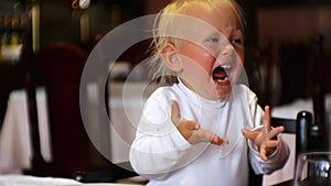 Baby eating food in restaurant. Caucasian blue-eyed child in highchair eats too spicy food and screams with surprise