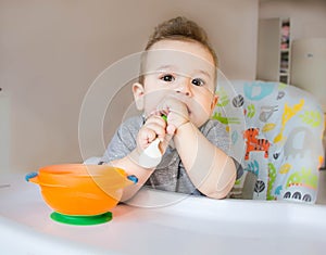 Baby eating food with a spoon, toddler eating messy and getting dirty infant having oatmeal as breakfast