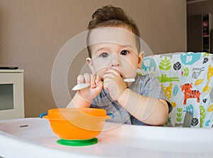 Baby eating food with a spoon, toddler eating messy and getting dirty, infant having oatmeal as breakfast