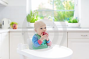 Baby boy eating apple in white kitchen at home